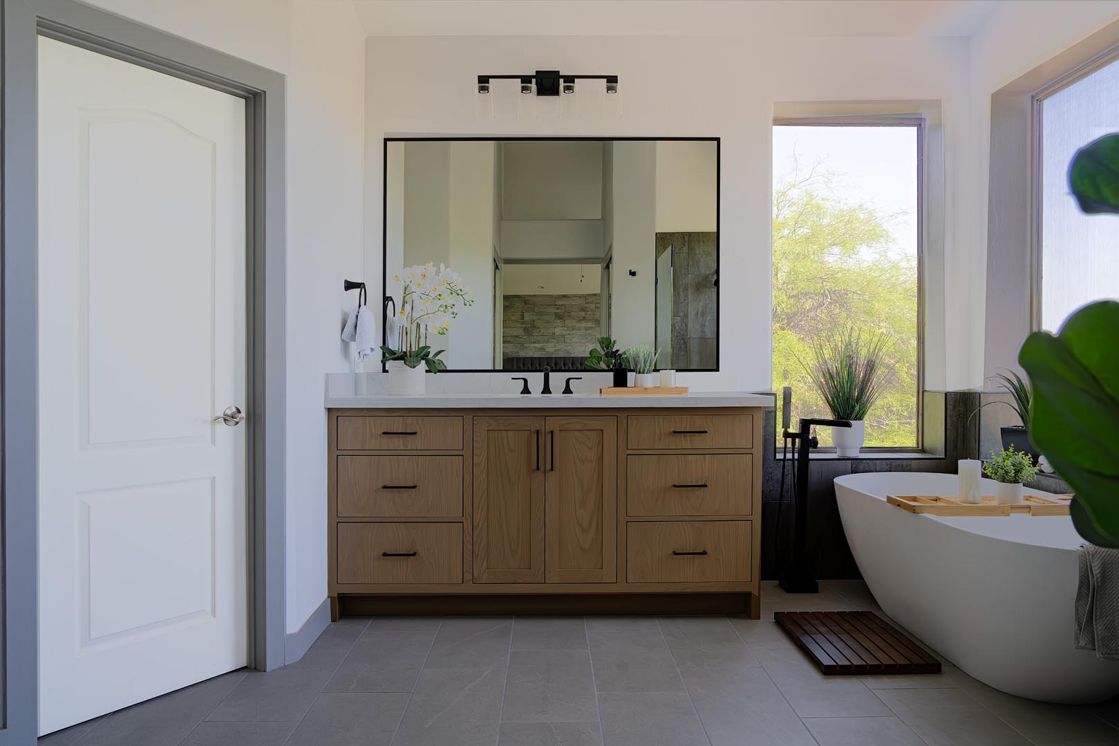 Remodeled primary bathroom with a white oak vanity, black fixtures and a freestanding tub
