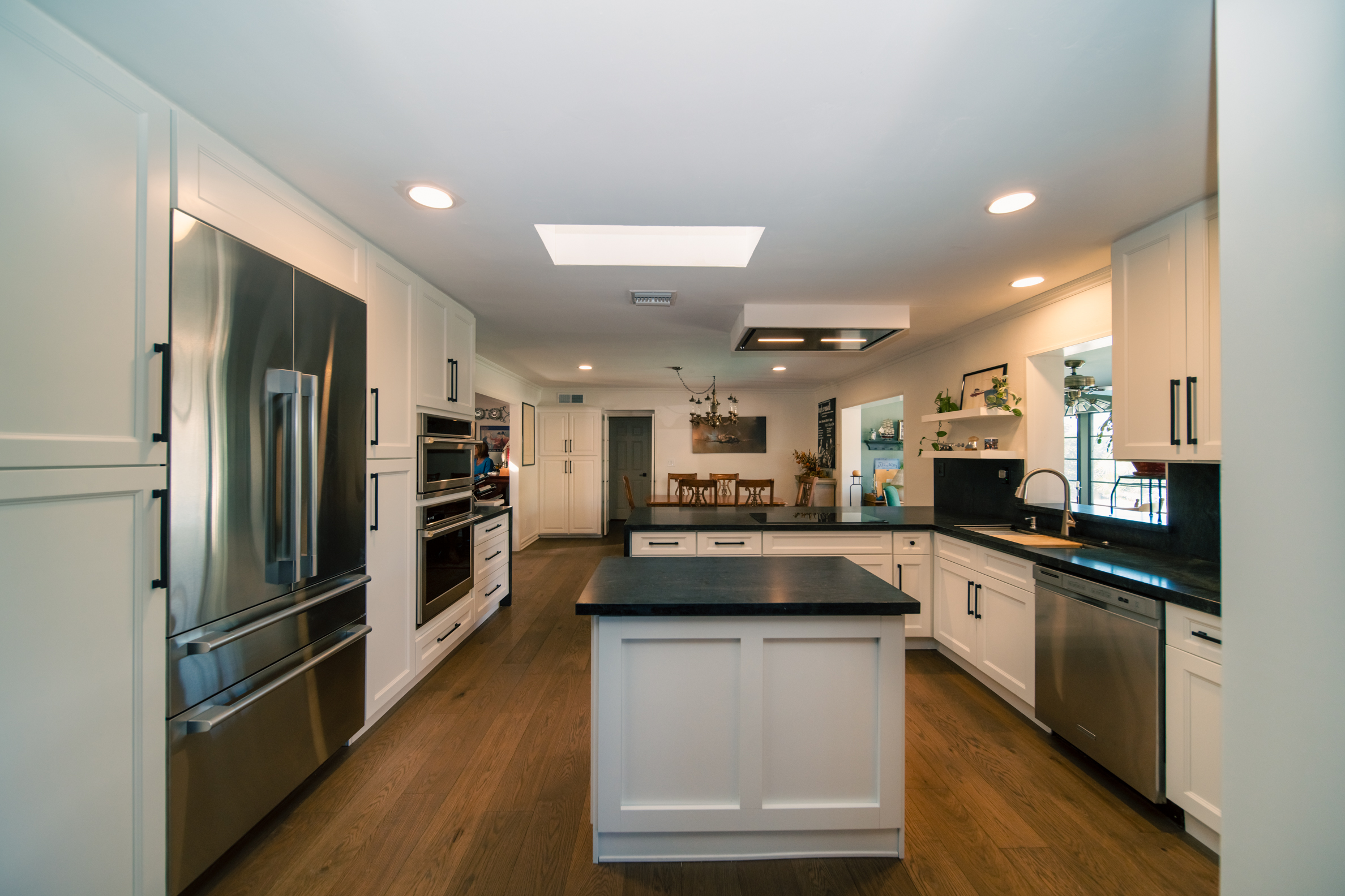 Open plan kitchen remodel with white shaker cabinetry, dark stone counters and oak flooring